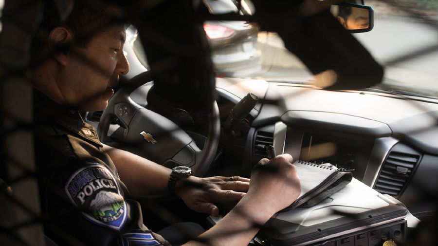Officer Ron writing in a all weather notebook inside the cab of his police car.