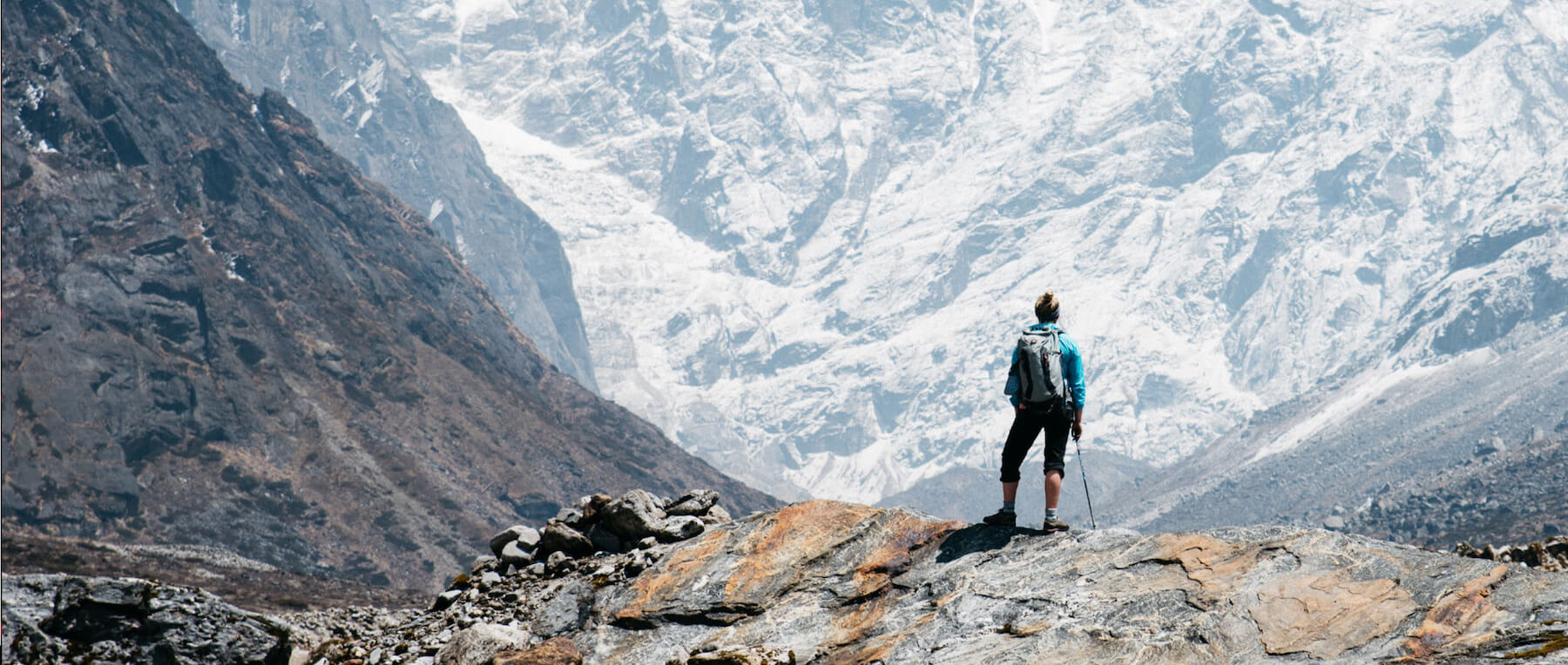 mountaineer on the edge of a cliff looking at a glacier
